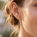 Extreme close-up of a smiling model wearing a delicate King Gold 18k yellow gold twisted halo stud earring.
تصوير ماكرو قريب لحلق بريمة دهب عيار 18 بتصميم مجدول من كينج جولد على موديل مبتسمة