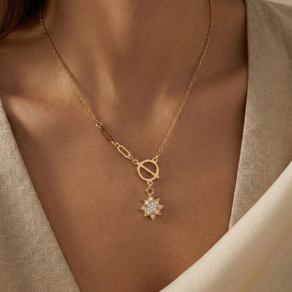 Gold necklace with a star-shaped pendant on a person wearing a beige outfit.