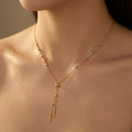 Gold necklace with dangling beads on a person's neck against a neutral background