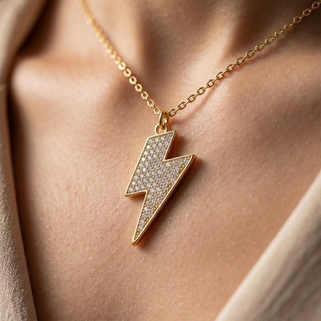 Macro close-up of a Fine gold 18k yellow gold lightning bolt pendant on a model's collarbone, highlighting the intricate pave stones and polished metal edges.
لقطة ماكرو مقربة لقلادة فاين جولد (Fine gold) بتصميم صاعقة البرق من الذهب الأصفر عيار 18 على عظمة ترقوة عارضة أزياء، تبرز تفاصيل الفصوص الدقيقة وحواف المعدن اللامعة.