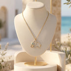 A gold elephant pendant necklace with diamond accents and a turquoise eye, displayed on a cream-colored jewelry bust. The background features a sunny, Mediterranean-style patio with arches, olive branches, and a soft-focus view of the blue ocean.
قلادة ذهبية بدلاية على شكل فيل مزينة بقطع من الألماس وعين تركوازية، معروضة على تمثال نصفي للمجوهرات بلون كريمي. تظهر في الخلفية شرفة مشمسة على طراز البحر الأبيض المتوسط مع أقواس، وأوراق زيتون، وإطلالة ناعمة للمحيط الأزرق.