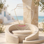 18K gold necklace with fuchsia pink gemstone pendant on a clear acrylic bust stand, set against a Mediterranean-style background.
سلسلة ذهب عيار ١٨ مع دلاية بأحجار فوشيا بينك على ستاند عرض أكريليك شفاف، في خلفية مستوحاة من أجواء البحر المتوسط.