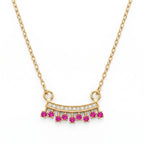 18K gold fringe necklace with clear pavé stones and seven vibrant fuchsia pink gemstones laid flat on a white marble surface.
سلسلة ذهب عيار ١٨ مع دلاية بأحجار شفافة بريليانت و٧ أحجار فوشيا بينك زاهية، معروضة بشكل مسطح على سطح رخام أبيض.