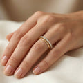 Soft-focus photograph of a woman's hand resting on warm white silk fabric, elegantly modeling a slim Fine Gold 18k yellow gold wedding promise ring paired with a classic gold band. This delicate diamond half-eternity ring belongs to The Forever Edit category, showcasing a timeless bridal aesthetic.