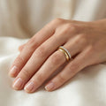 Soft-focus lifestyle photograph of a woman's hand resting gracefully on warm ivory silk fabric, elegantly modeling a slim Remas 18k yellow gold promise ring paired perfectly with a classic gold wedding band. Part of The Forever Edit category, this delicate 13-stone half-eternity ring highlights a timeless and harmonious bridal aesthetic.