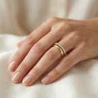 Soft-focus lifestyle photograph of a woman's hand resting gracefully on warm ivory silk fabric, elegantly modeling a slim Remas 18k yellow gold promise ring paired perfectly with a classic gold wedding band. Part of The Forever Edit category, this delicate 13-stone half-eternity ring highlights a timeless and harmonious bridal aesthetic.