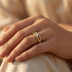 Hand wearing a gold ring with a diamond design on a soft beige background
