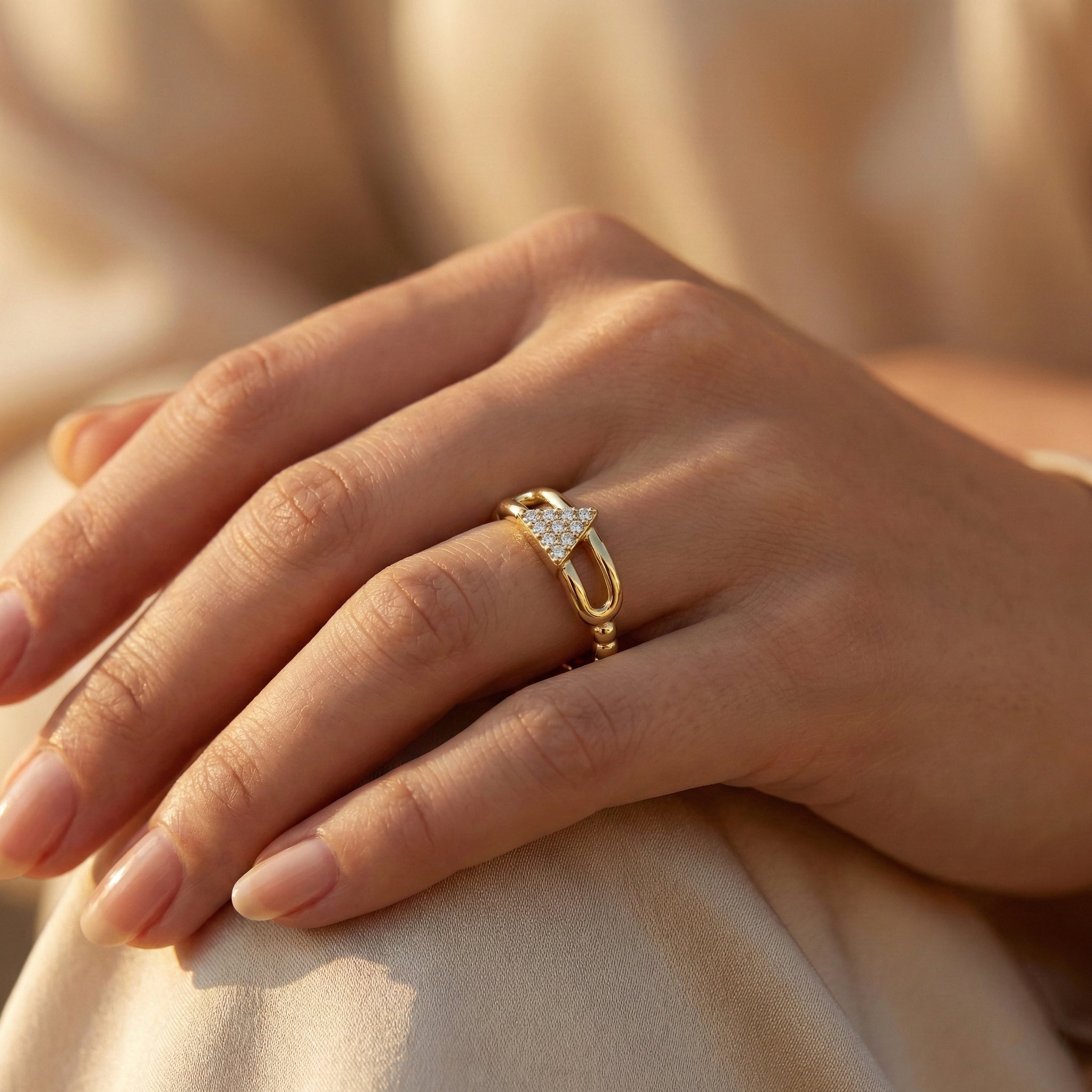 Hand wearing a gold ring with a diamond design on a soft beige background
