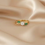 Gold ring with a diamond and emeralds on beige satin fabric