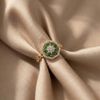 Gold ring with green gemstones on beige fabric