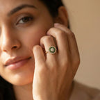 Close-up of a woman's hand wearing a green gemstone ring on a neutral background