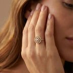 Close-up of a woman's hand wearing a gold ring with a diamond design, touching her face.