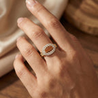 Close-up of a hand wearing an ornate ring with a brown gemstone on a neutral background