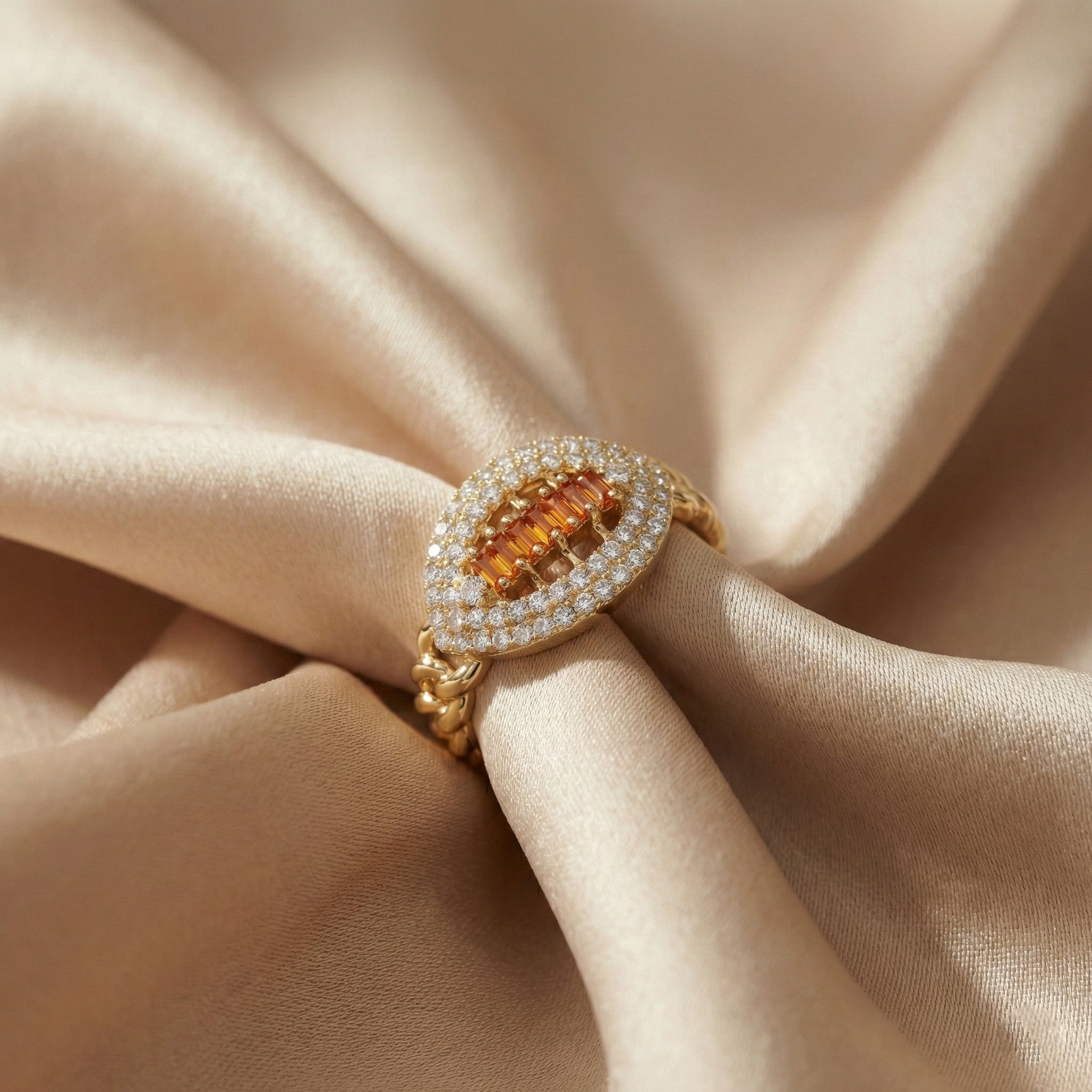 Gold ring with orange gemstone and diamond accents on beige fabric