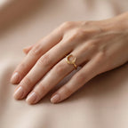 Lamar 18k yellow gold crescent moon ring worn delicately on the ring finger of an elegant feminine hand, resting against a soft, smooth beige backdrop in warm luxury lighting.