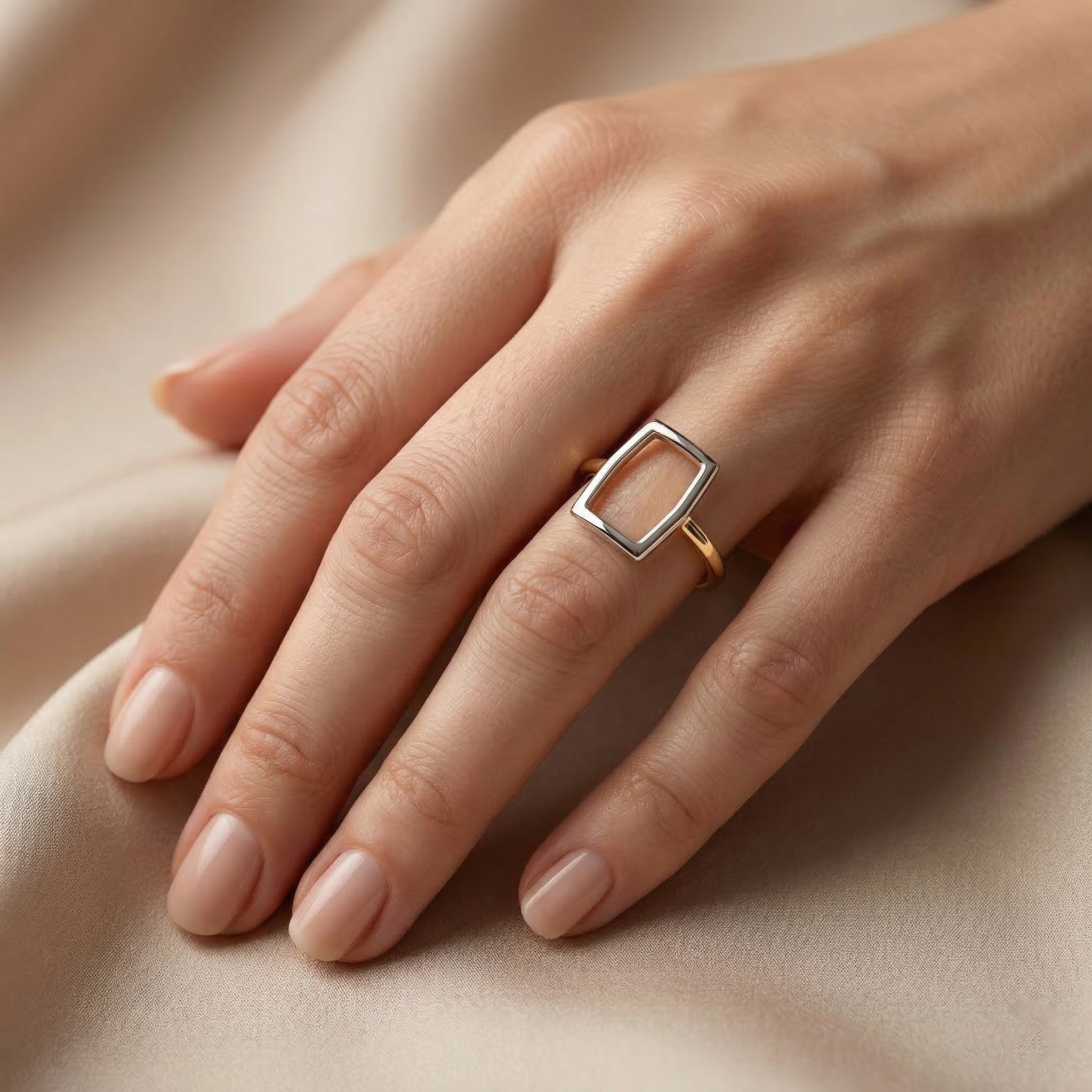 Alyans 18k yellow gold geometric ring worn on the ring finger of an elegant feminine hand, resting against a smooth, soft beige backdrop in warm, diffused luxury lighting.