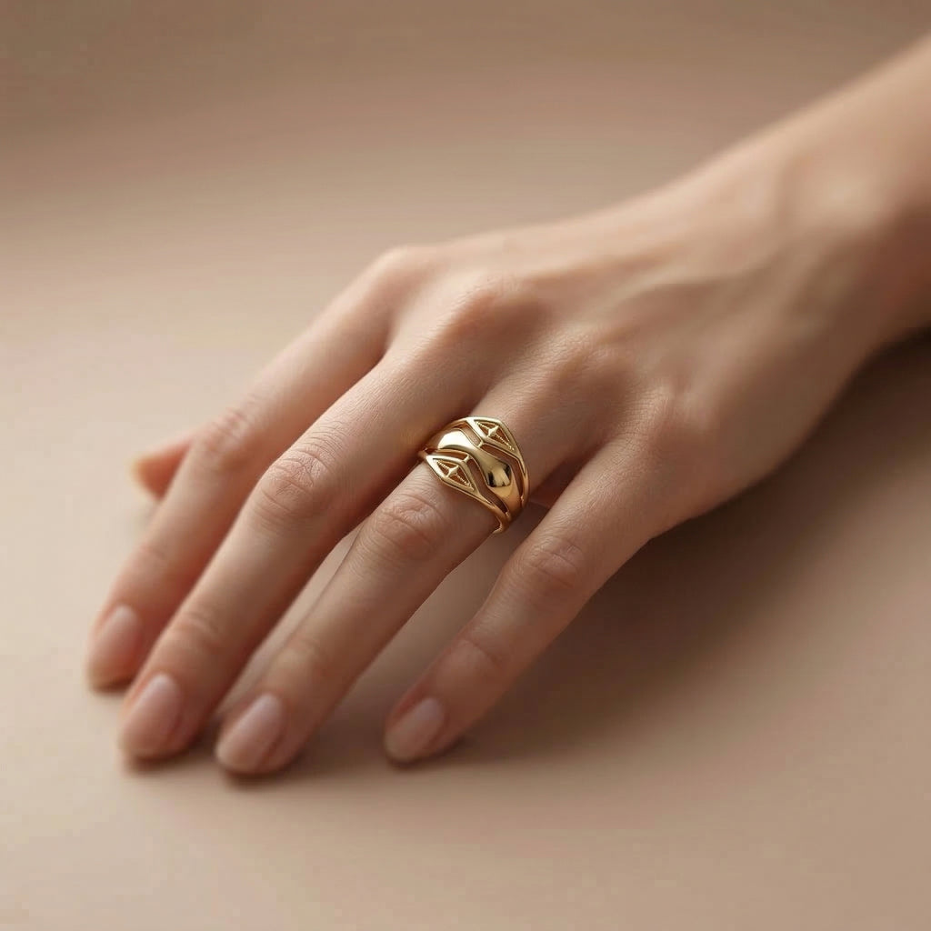 A luxury lifestyle photograph featuring an Andria 18k yellow gold ring worn elegantly on a feminine ring finger, set against a soft beige backdrop to emphasize the refined, organic woven design.