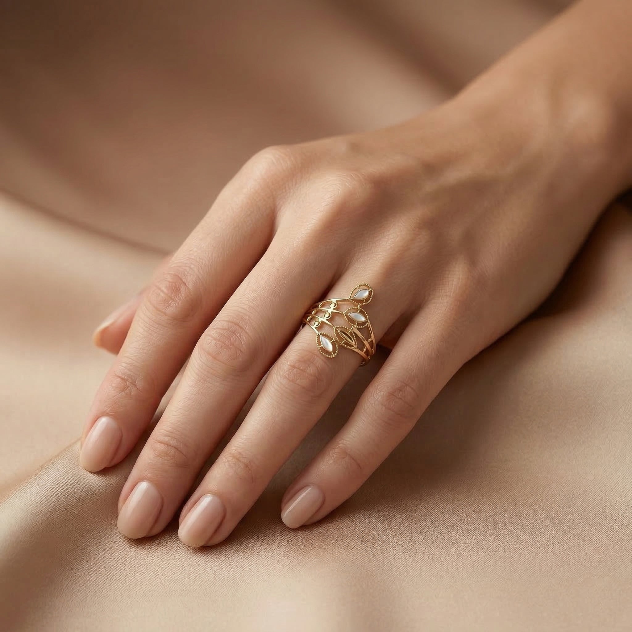 Andria 18k yellow gold botanical ring worn elegantly on the ring finger of a feminine hand, resting gracefully against a smooth, soft beige backdrop in warm luxury lighting.