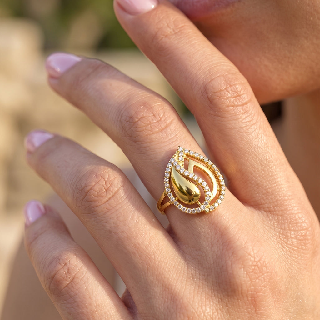 Close-up of a feminine hand gracefully modeling a Fine Gold 18k yellow gold ring with sparkling stones, set against a creamy, dreamy bokeh background. لقطة قريبة ليد أنثوية ترتدي خاتم ذهب عيار 18 من فاين جولد يبرز دقة التفاصيل ولمعان الفصوص، مع خلفية ناعمة وضبابية.