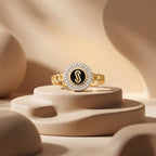 Loaloaa 18k yellow gold chain-link ring with a black enamel center displayed on smooth beige sculptural pedestals under soft luxury studio lighting. خاتم ذهب عيار 18 من لؤلؤة معروض بشكل فني على منصات بيج ناعمة تحت إضاءة استوديو فاخرة تبرز تفاصيل الخاتم.
