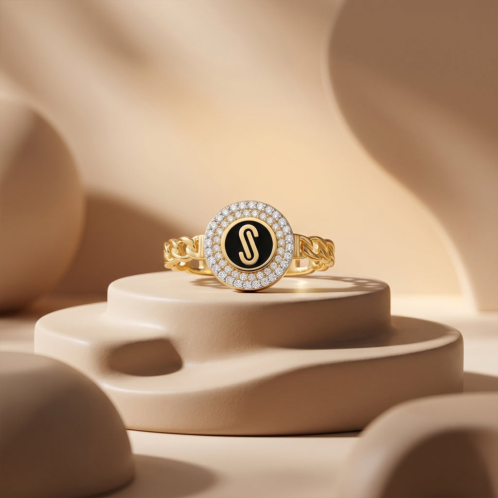 Loaloaa 18k yellow gold chain-link ring with a black enamel center displayed on smooth beige sculptural pedestals under soft luxury studio lighting. خاتم ذهب عيار 18 من لؤلؤة معروض بشكل فني على منصات بيج ناعمة تحت إضاءة استوديو فاخرة تبرز تفاصيل الخاتم.
