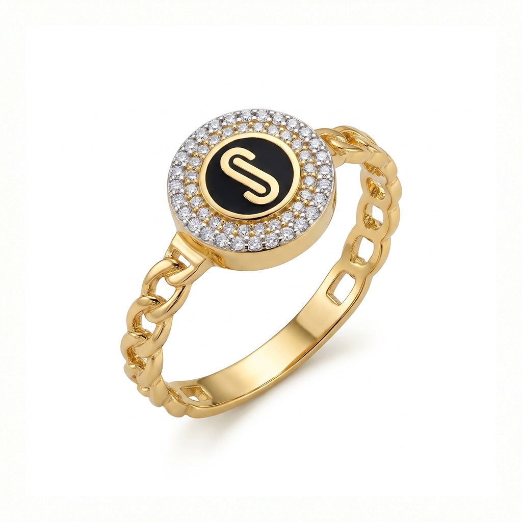 Loaloaa 18k yellow gold chain-link ring featuring a round black enamel center with a gold initial surrounded by sparkling stones, on a pure white background. خاتم ذهب عيار 18 من لؤلؤة بتصميم جنزير وجزء دائري مطلي بالمينا السوداء مع حرف بالذهب وحوله فصوص، على خلفية بيضاء نقية.