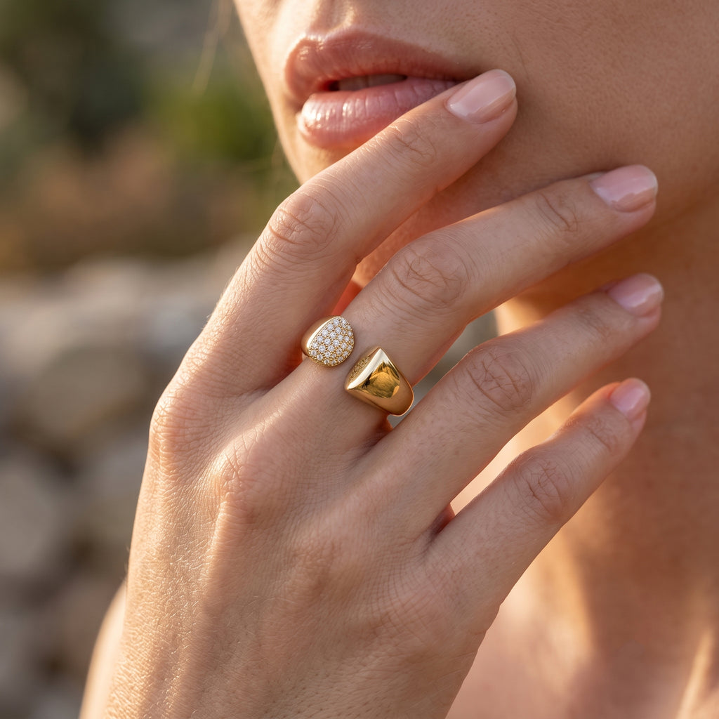 Close-up macro shot of the UNO 18k yellow gold open ring on a woman's hand, showcasing the sharp contrast between the radiant stones and polished gold.
صورة قريبة جداً لخاتم أونو المفتوح عيار 18 على إيد موديل، بتبرز التباين بين لمعة الدهب والفصوص.