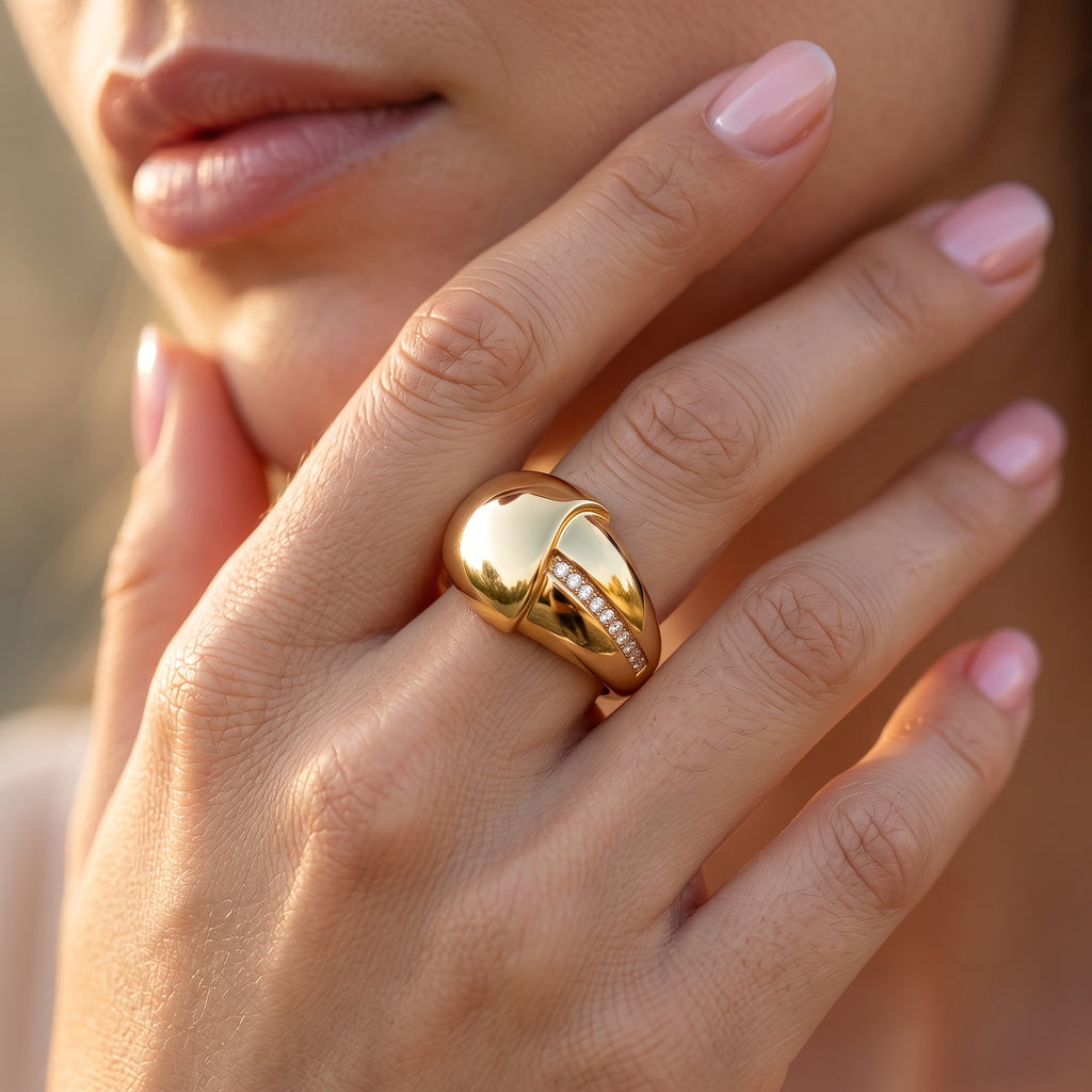 Close-up macro shot of the UNO 18k yellow gold crossover ring on a woman's hand, highlighting the soft golden reflections and the diagonal channel of sparkling stones.
قطة قريبة لخاتم أونو المتداخل دهب عيار 18 على إيد موديل، بتبرز لمعان الدهب والفصوص المترصة بشكل مائل.