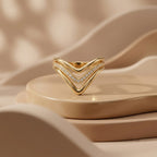UNO 18k yellow gold V-shaped ring displayed upside down on modern beige curved pedestals under soft luxury studio lighting.
خاتم أونو دهب عيار 18 بتصميم V معروض بشكل مقلوب على قواعد بيج فخمة وتصميم مودرن.