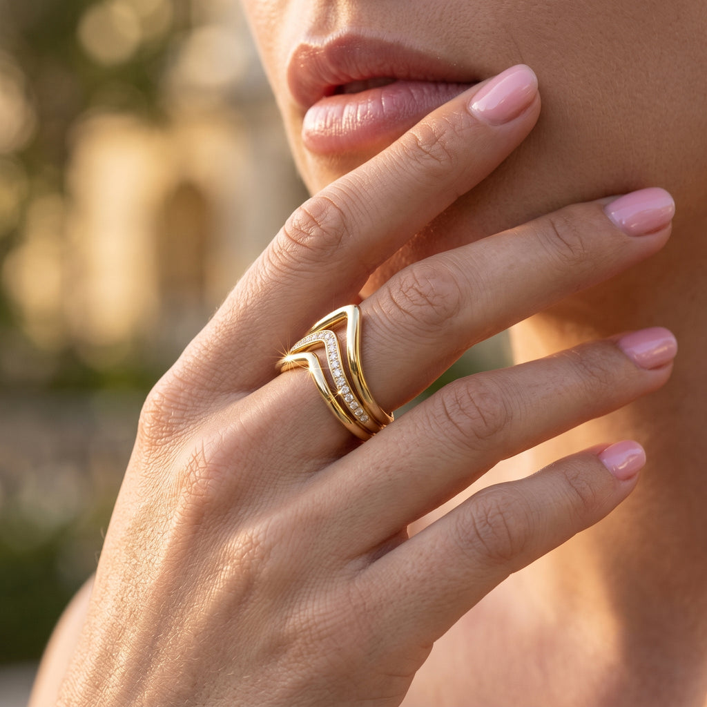 Close-up macro shot of the UNO 18k yellow gold V-shaped ring pointing elegantly downwards on a woman's hand, highlighting the sharp geometric design and sparkling center band.
صورة قريبة جداً (ماكرو) لخاتم أونو بتصميم السبعة مقلوب لتحت على إيد موديل، بتبرز شكل الـ V والفصوص اللي بتلمع في النص.