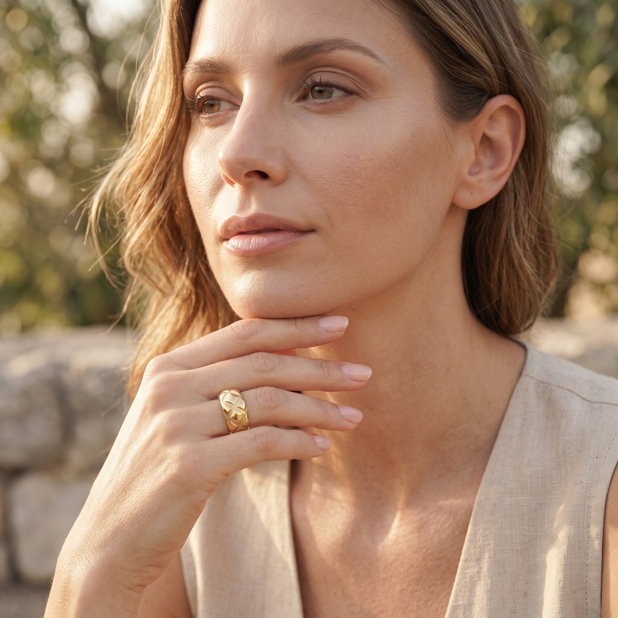 Elegant woman outdoors wearing the UNO 18k yellow gold quilted ring, softly resting her hand near her chin in warm, natural daylight.
موديل شيك لابسة خاتم أونو الدهب بنقشة المربعات المتقاطعة في إضاءة نهارية طبيعية
