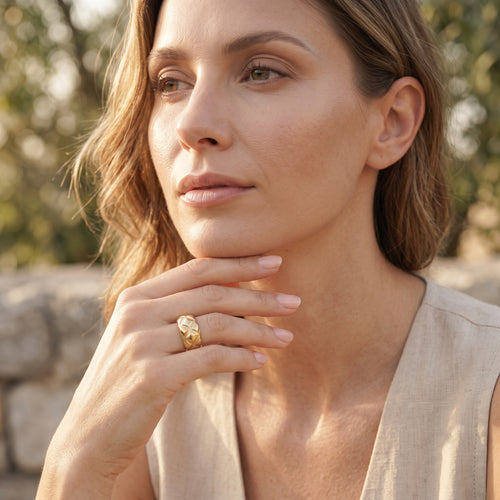 Elegant woman outdoors wearing the UNO 18k yellow gold quilted ring, softly resting her hand near her chin in warm, natural daylight.
موديل شيك لابسة خاتم أونو الدهب بنقشة المربعات المتقاطعة في إضاءة نهارية طبيعية