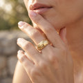 Close-up macro shot of the UNO 18k yellow gold quilted ring on a woman's hand, showcasing the engraved diamond-shape pattern catching the golden sunlight.
صورة قريبة جداً لخاتم أونو الدهب عيار 18 بالنقشة الهندسية على إيد موديل في إضاءة الشمس الدافية.