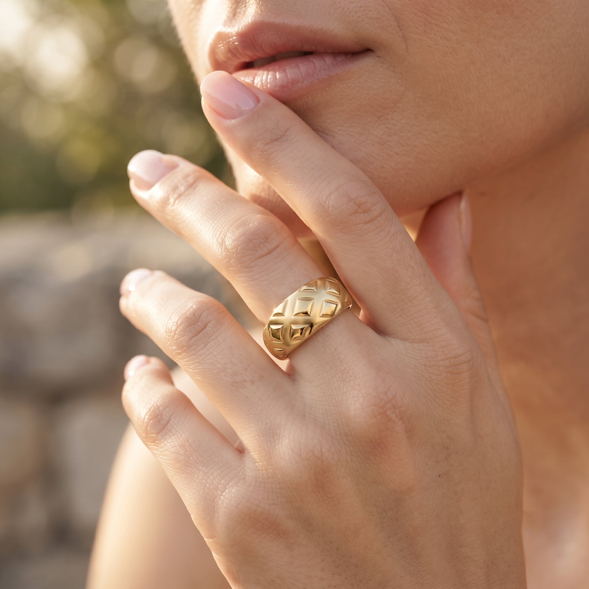 Close-up macro shot of the UNO 18k yellow gold quilted ring on a woman's hand, showcasing the engraved diamond-shape pattern catching the golden sunlight.
صورة قريبة جداً لخاتم أونو الدهب عيار 18 بالنقشة الهندسية على إيد موديل في إضاءة الشمس الدافية.