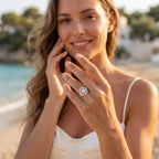 Lifestyle campaign portrait of a woman in an ivory dress wearing the Egypt Gold 7.61g floral white gold twin ring set on a sunny Mediterranean beach.	صورة لعارضة أزياء ترتدي فستان عاجي وطقم خواتم توينز ذهب أبيض بتصميم وردة من إيجيبت جولد بوزن 7.61 جرام على شاطئ متوسطي مشمس.