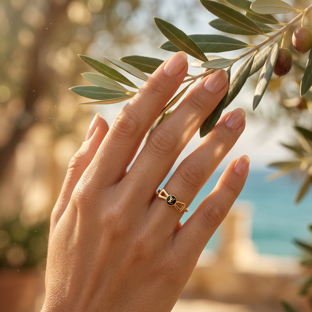 18k yellow gold Lamar bow ring worn on a graceful hand gently touching a Mediterranean olive branch at golden hour.	خاتم فيونكة من الذهب الأصفر عيار 18 من لامار على يد ناعمة تلمس غصن زيتون بلطف وقت الساعة الذهبية.