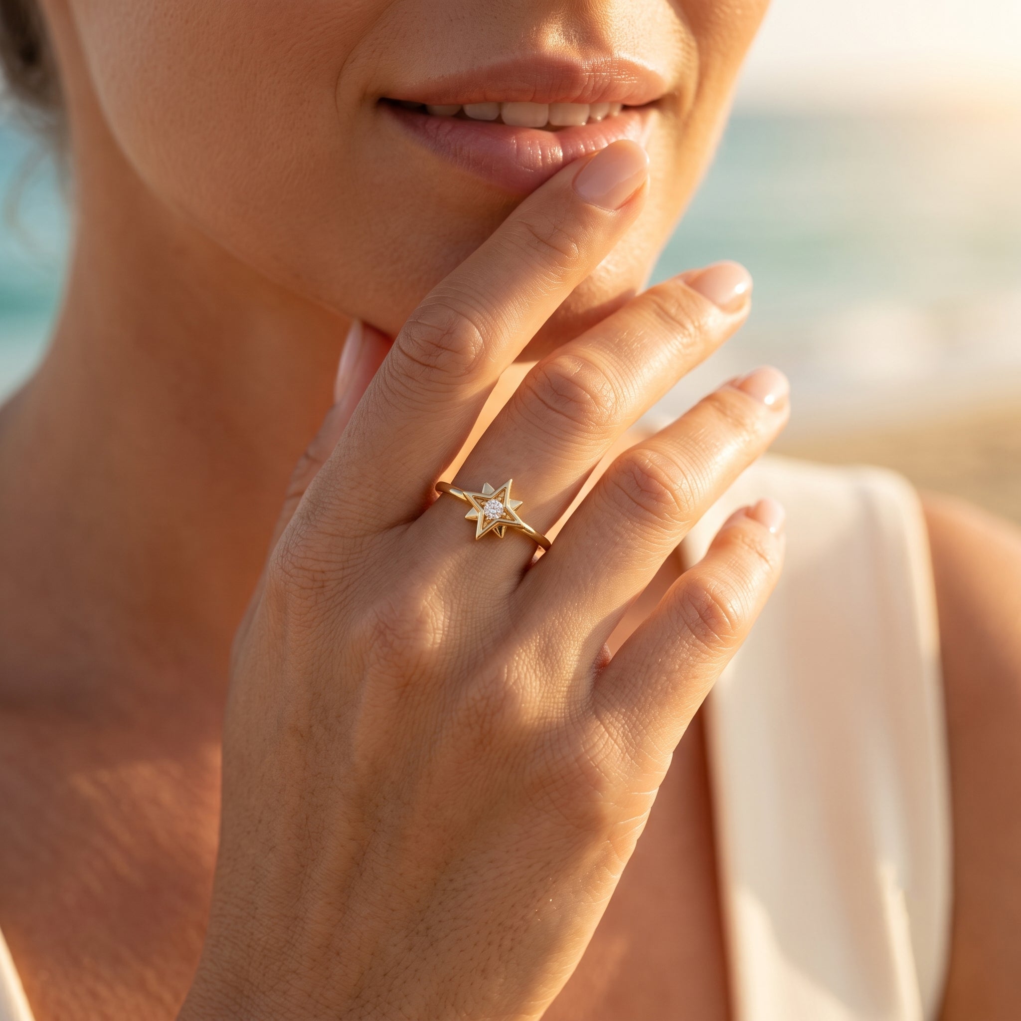 A soft lifestyle close-up of a woman resting her hand near her lips at sunset, showcasing an 18k yellow gold star ring by Remas Gold against a blurred beach background.	صورة مقربة ناعمة لامرأة تضع يدها بالقرب من شفتيها عند غروب الشمس، وتستعرض خاتم نجمة من الذهب الأصفر عيار 18 من ريماس جولد مع خلفية شاطئ مشوشة.