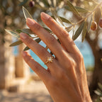 Extreme macro editorial shot of a delicate 1.10g 18k yellow gold star ring by Remas Gold on a woman's hand gently touching an olive branch. صورة مقربة جداً ليد امرأة ترتدي خاتم نجمة من الذهب الأصفر عيار 18 من ريماس جولد بوزن 1.10 جم وتلمس غصن زيتون برقة.