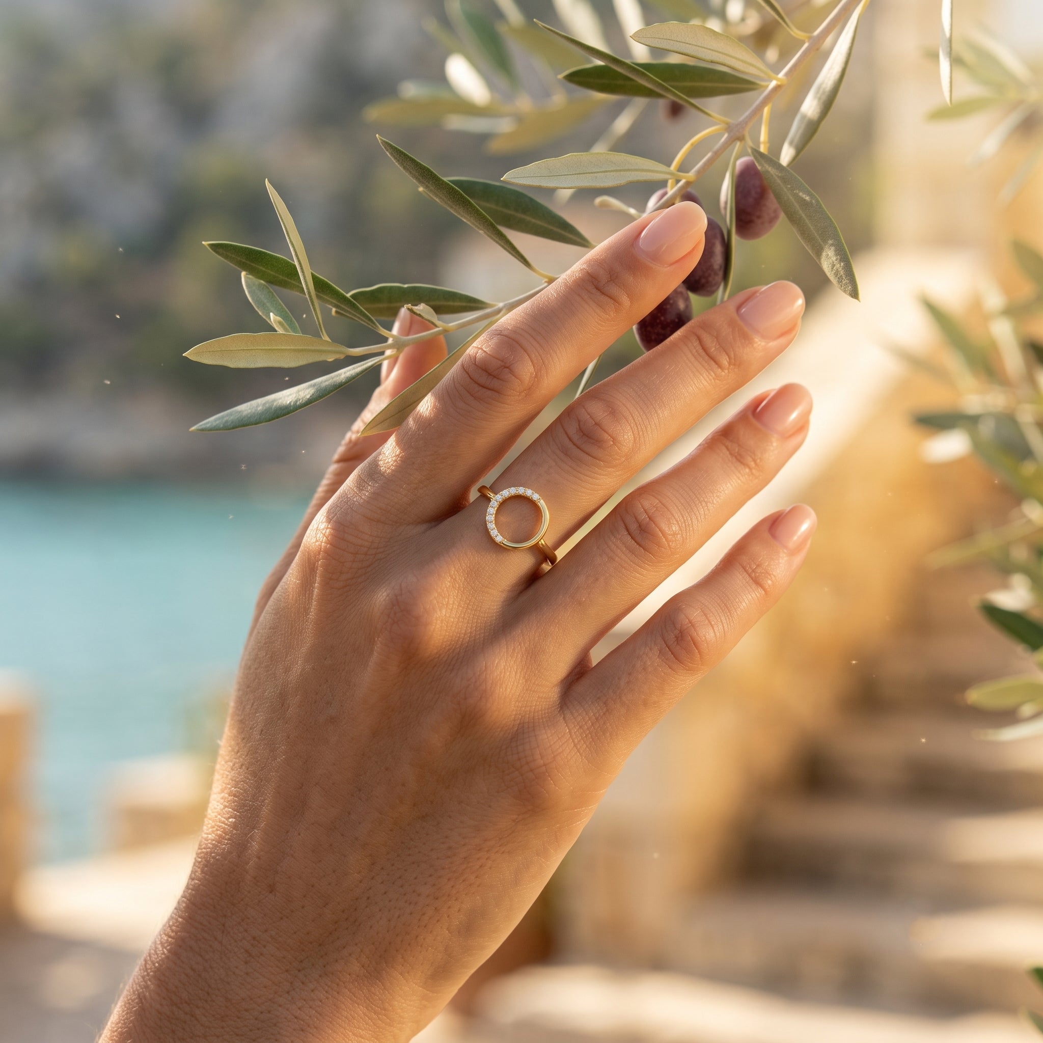 Macro lifestyle shot of the King Gold open circle ring, 18k gold, on a hand gently touching an olive branch.	لقطة مقربة لخاتم كينج جولد الدائري، ذهب عيار 18، على يد تلمس غصن زيتون بلطف.
