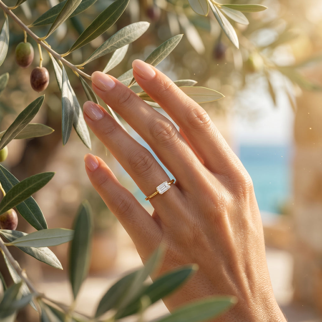 Close-up of the delicate Andria 18k gold ring on a hand gently touching a Mediterranean olive branch.	لقطة مقربة لخاتم أندريا الرقيق من الذهب عيار 18 على يد تلمس غصن زيتون متوسطي بلطف.