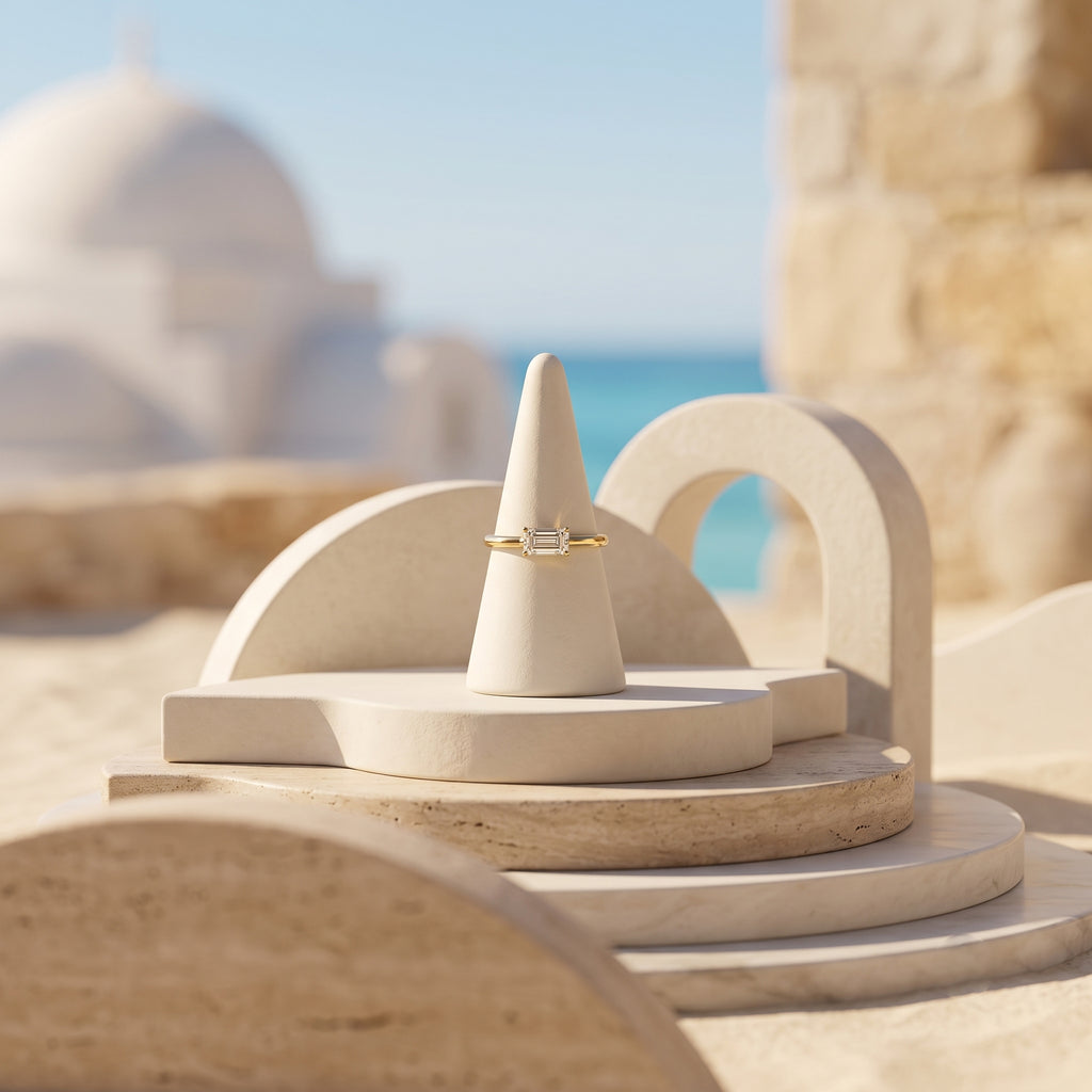 Andria 18k gold white stone ring displayed on an elegant travertine pedestal with a coastal Mediterranean background.	خاتم أندريا من الذهب عيار 18 بفص أبيض معروض على منصة حجرية أنيقة مع خلفية ساحلية متوسطية.