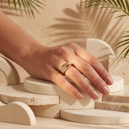 Fine Gold 18k yellow gold pavé ring (4.55g) on a feminine hand resting on a sculptural plaster pedestal with tropical palm shadows. خاتم فاين جولد ذهب عيار 18 (4.55 جرام) على يد رقيقة تستريح على منصة منحوتة مع ظلال أوراق النخيل الاستوائية.
