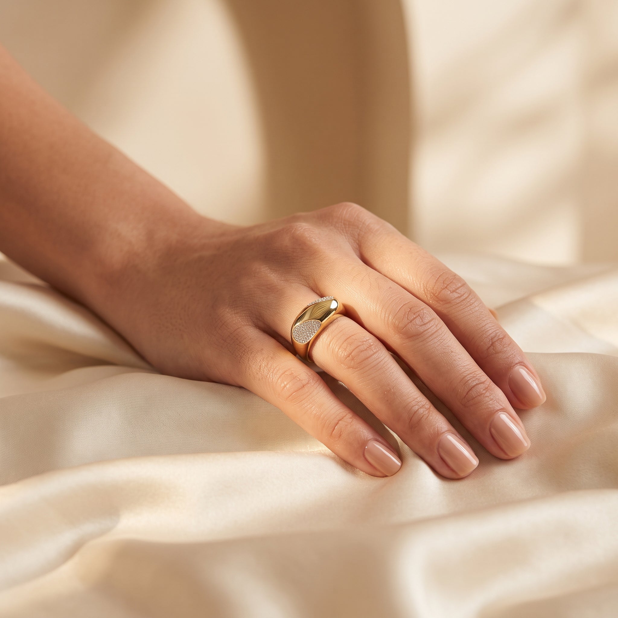 Fine Gold 18k yellow gold pavé dome ring weighing 4.55g worn on a woman's hand resting on luxurious warm ivory silk. خاتم فاين جولد ذهب عيار 18 بومبيه بوزن 4.55 جرام ترتديه امرأة ويدها تستريح على قماش حرير عاجي دافئ وفاخر.