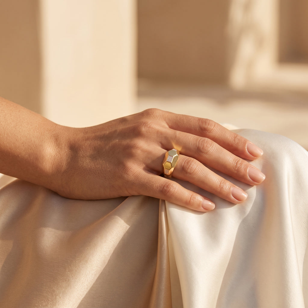 Remas Gold 18k yellow gold faceted ring (2.93g) on a feminine hand resting elegantly on warm ivory silk. خاتم ريماس جولد مضلع عيار 18 (2.93 جرام) على يد رقيقة تستريح بأناقة على قماش حرير عاجي دافئ.