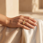 Remas Gold 18k yellow gold faceted ring (2.93g) on a feminine hand resting elegantly on warm ivory silk. خاتم ريماس جولد مضلع عيار 18 (2.93 جرام) على يد رقيقة تستريح بأناقة على قماش حرير عاجي دافئ.