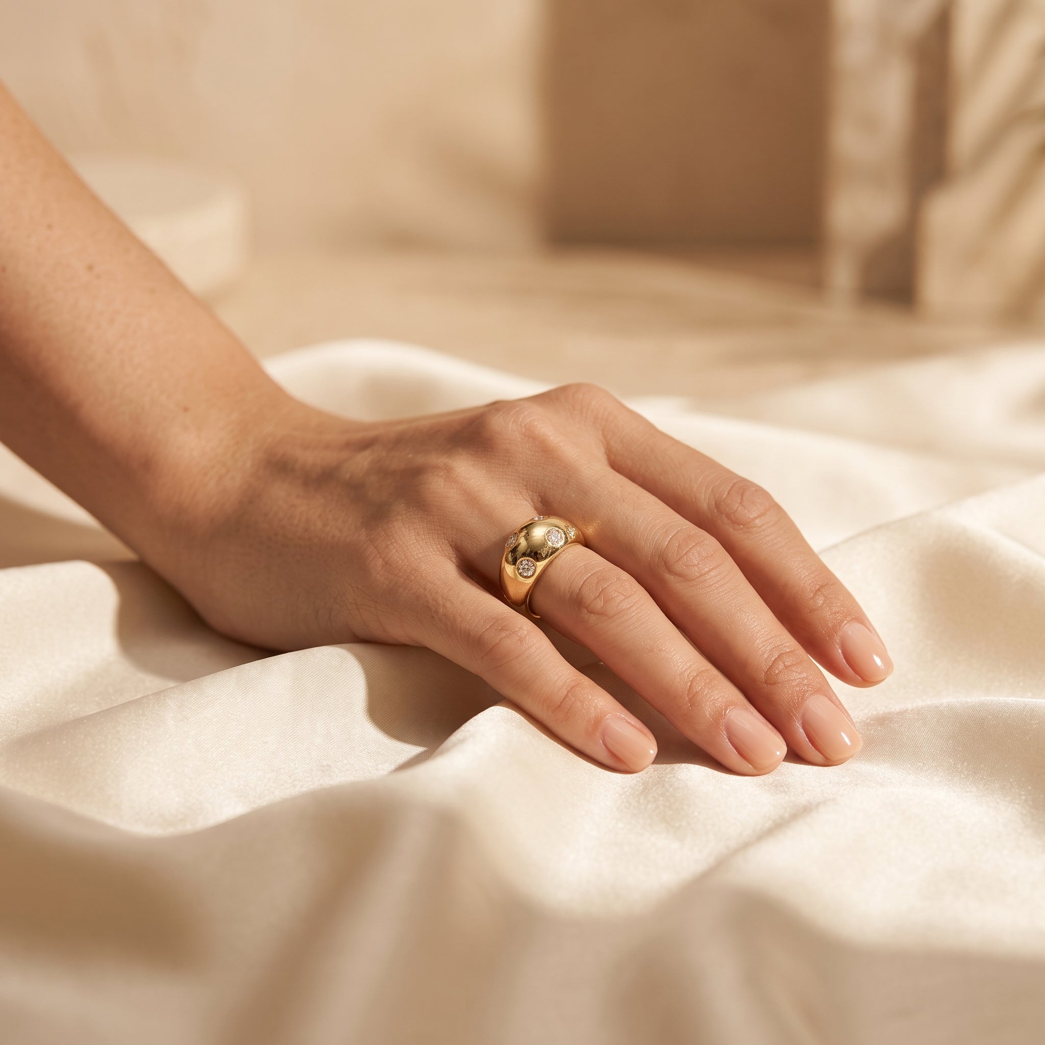 L'azurde 18k gold scattered gem ring (4g) on a woman's hand resting elegantly on warm ivory silk. خاتم لازوردي ذهب عيار 18 مرصع (4 جرام) على يد امرأة تستريح بأناقة على قماش حرير عاجي دافئ.