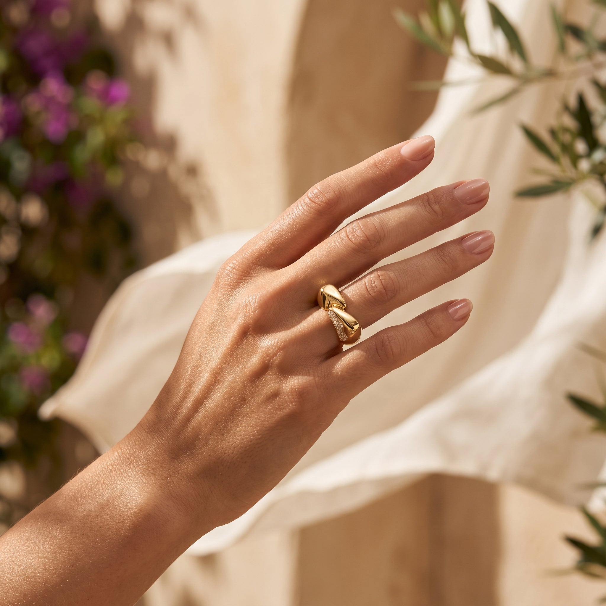 Close-up of a woman's hand in warm summer sunlight wearing a 5.37g L'azurde sculptural crossover ring. لقطة مقربة ليد امرأة في ضوء شمس الصيف الدافئ ترتدي خاتم لازوردي منحوت ومتقاطع بوزن 5.37 جرام.