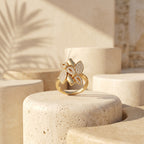 Fine Gold floral ring displayed elegantly on a minimalist ivory sculptural pedestal.	خاتم فاين جولد الذهبي معروض بأناقة على قاعدة نحتية عاجية بتصميم بسيط.