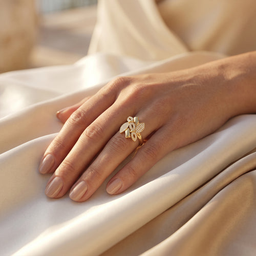 Fine Gold floral ring on a woman's hand resting gracefully on luxurious ivory silk.	خاتم فاين جولد الذهبي على يد امرأة تستريح بنعومة على قماش حرير عاجي فاخر.