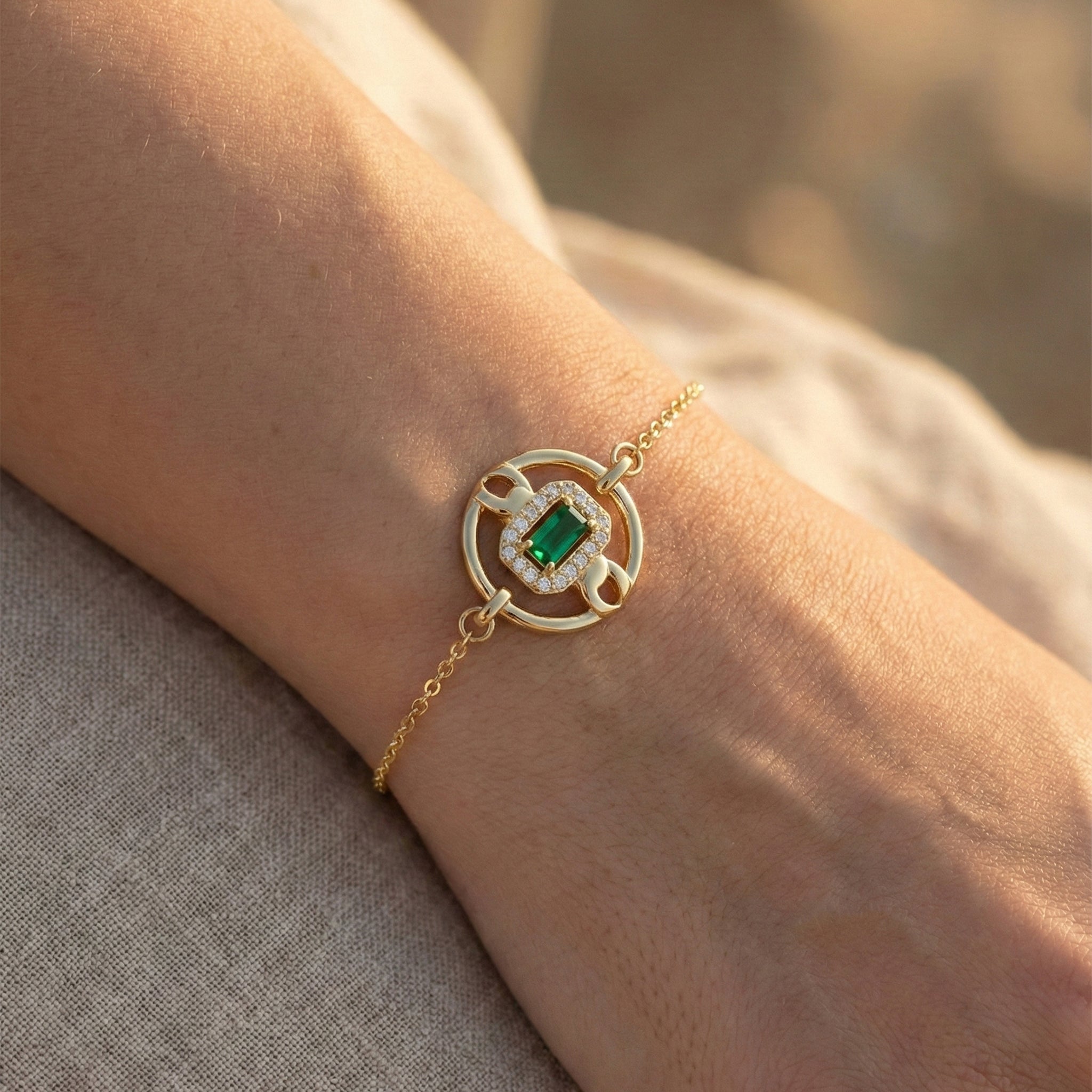 Gold bracelet with a green gemstone on a wrist against a neutral background